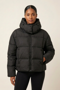 Front-facing close-up of the black puffer coat with the model in a new hand-in-pocket pose