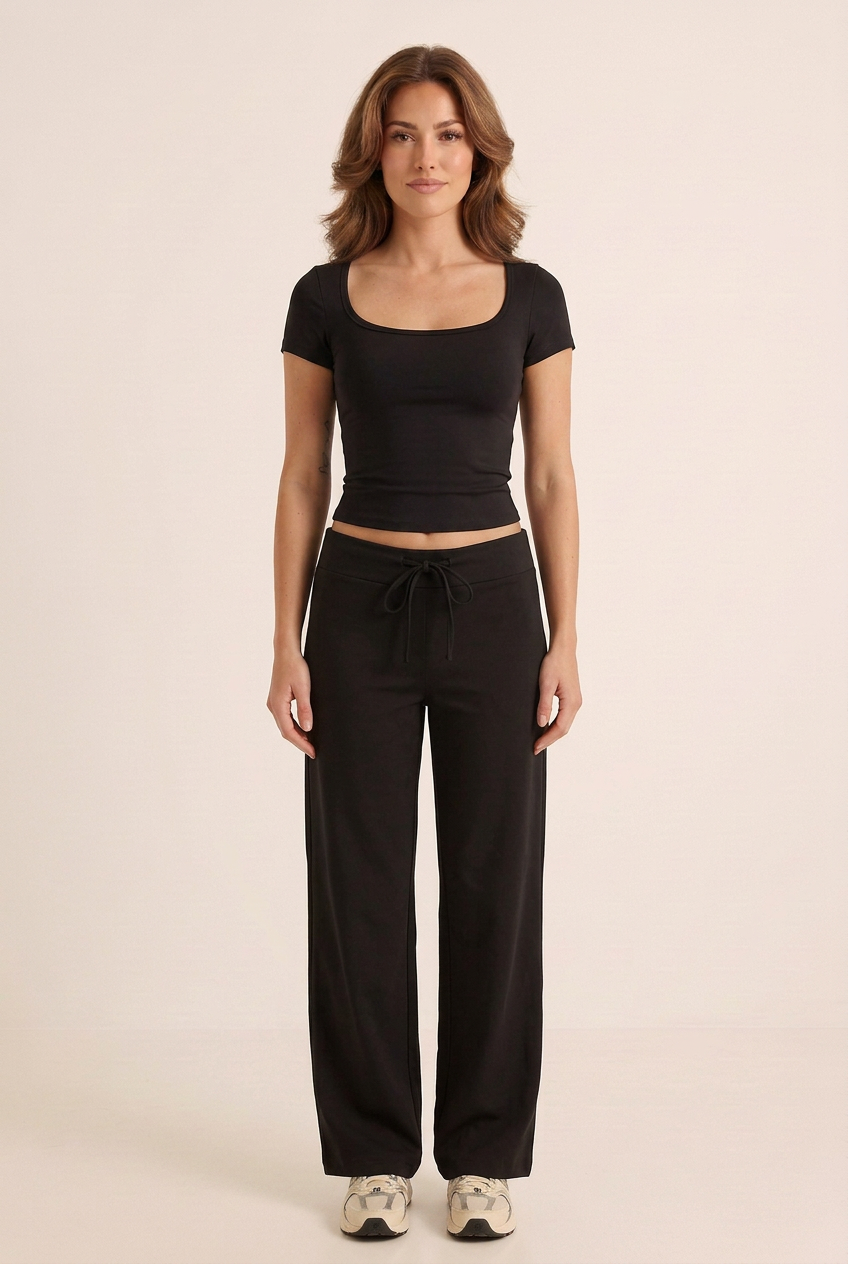 Front-facing studio image of the black short-sleeve top and wide-leg trouser set on the brunette model