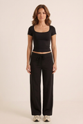 Front-facing studio image of the black short-sleeve top and wide-leg trouser set on the brunette model