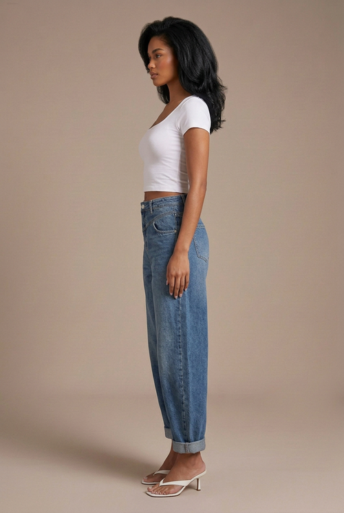 Side profile studio image of mixed-race model in blue balloon jeans, white tee, and white flip-flop kitten heels