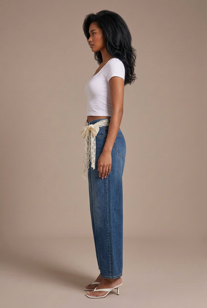 Side profile studio image of mixed-race model in dark indigo wide-leg jeans with lace waist wrap, white tee, and white kitten heels