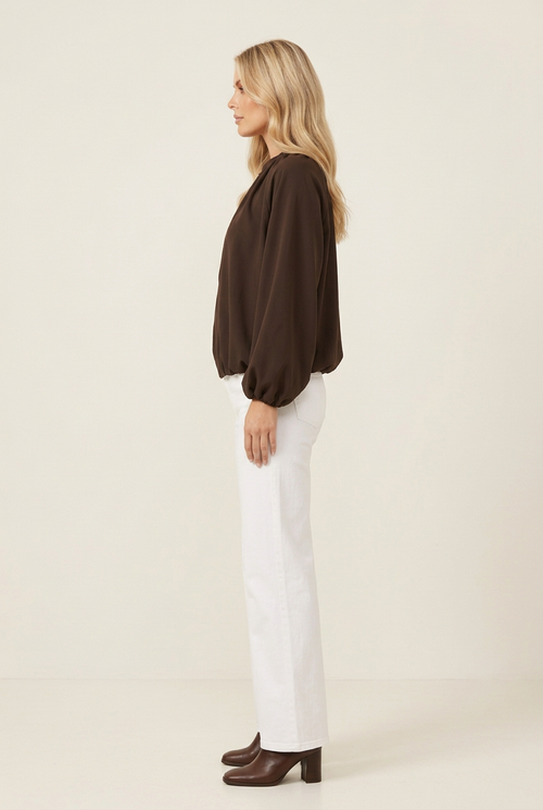 Side-profile studio image of the brown jacket with white wide-leg jeans and brown heeled boots