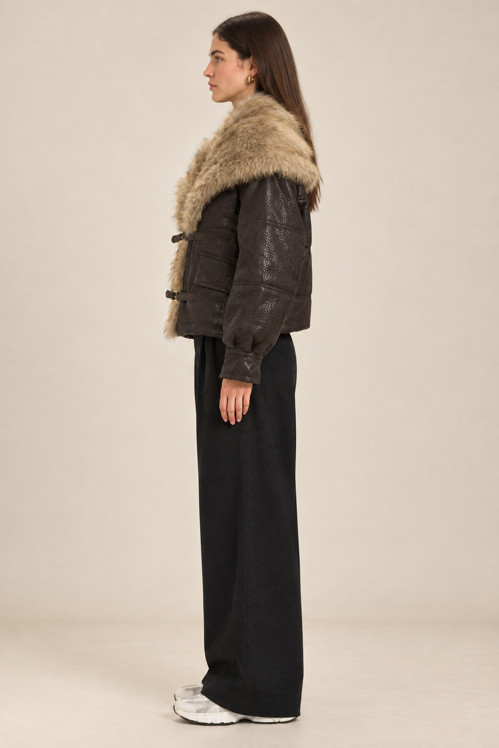 Side-profile studio image of the brunette model wearing the brown PU coat