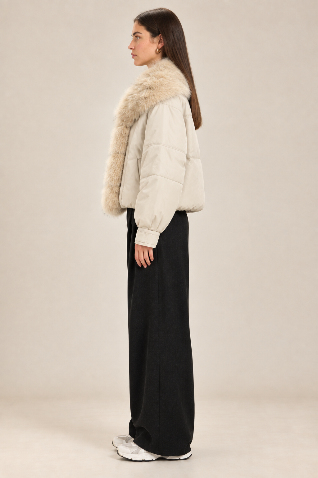 Side-profile studio image of the brunette model wearing the cream fur-trim jacket