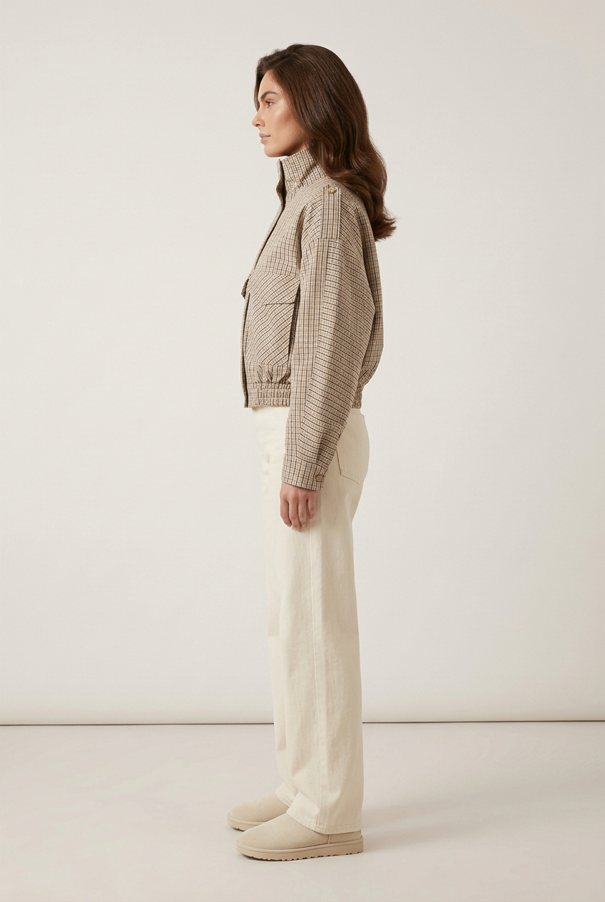 Side-profile studio view of the brunette model wearing the checked jacket, cream wide-leg jeans and cream Ugg-style boots