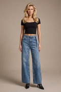 Studio image of blonde model in belted blue wide-leg jeans, black fitted square neck tee, and black leather boots
