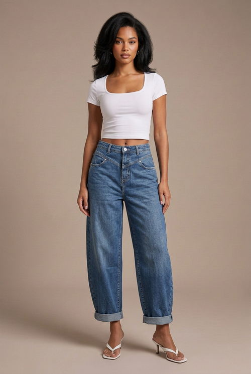 Studio image of mixed-race model with black blowout in blue balloon jeans, white fitted tee, and white flip-flop kitten heels