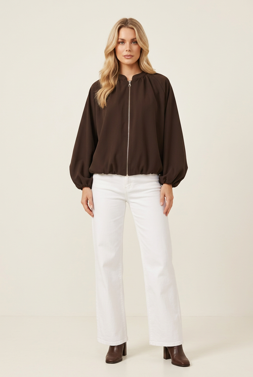 Studio image of the brown jacket with blonde blow-out hair, white wide-leg jeans and brown heeled boots